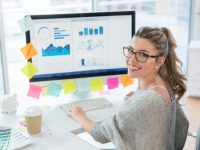 Woman working at the office on her computer and looking at the camera smiling