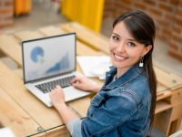 Happy female graphic designer working at the office using her laptop and looking at the camera smiling