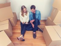 Young couple sitting in new house with packing boxes. They look like they have just moved in and they are very happy, smiling and talking. They are using a digital tablet, sitting on the floor in casual clothes. Copy space.